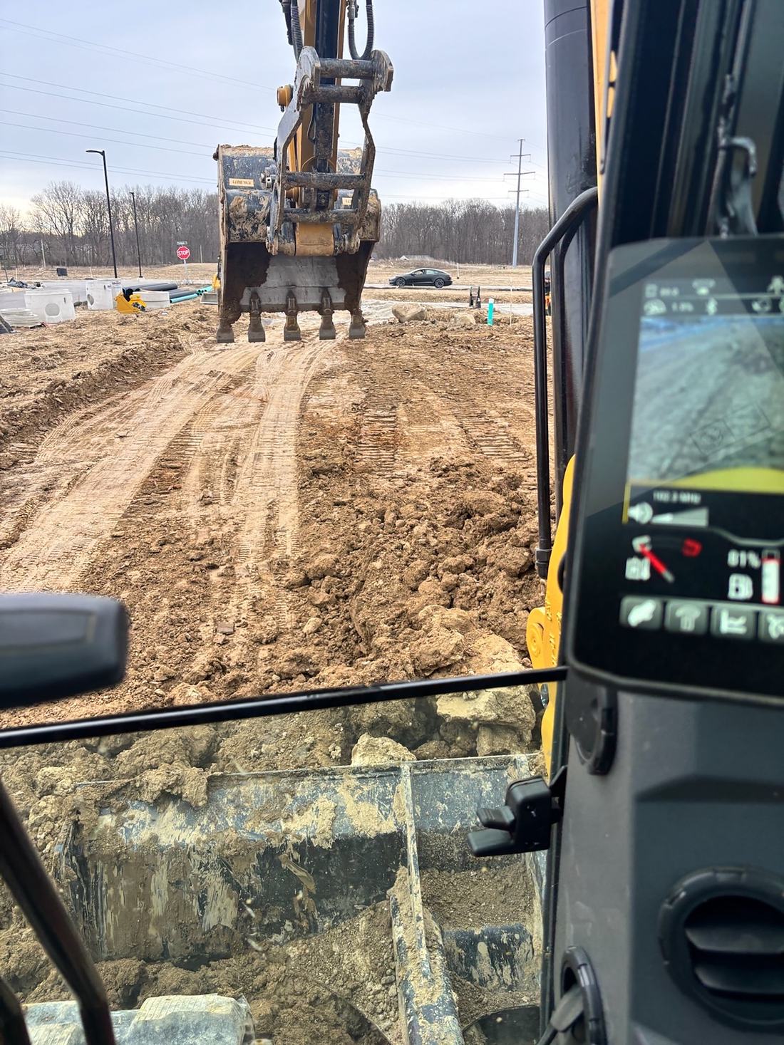 View from the BDX excavator cab of a loaded bucket on an active commercial site